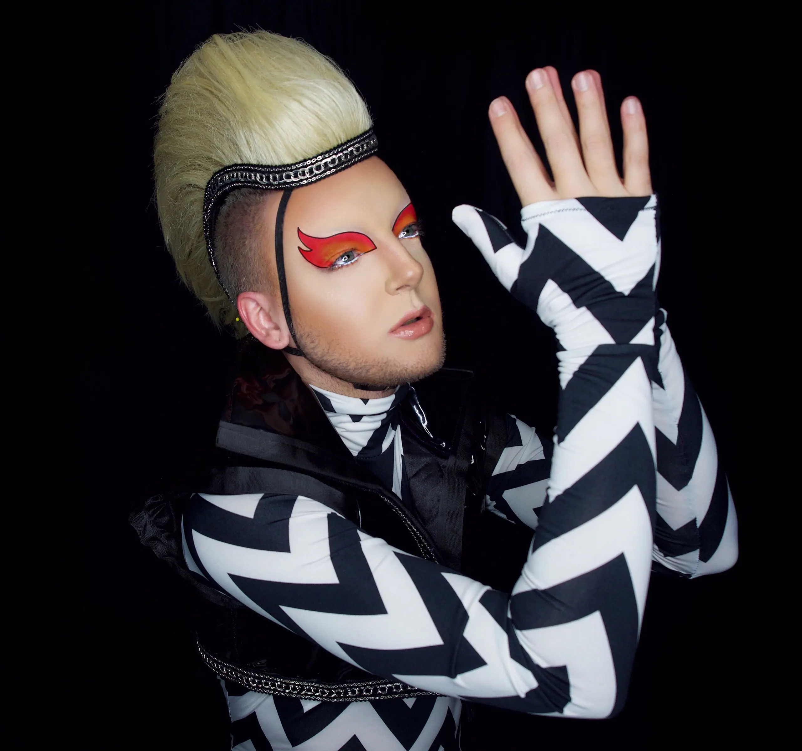Performer in a black and white chevron bodysuit with a tall blonde crest, hands raised