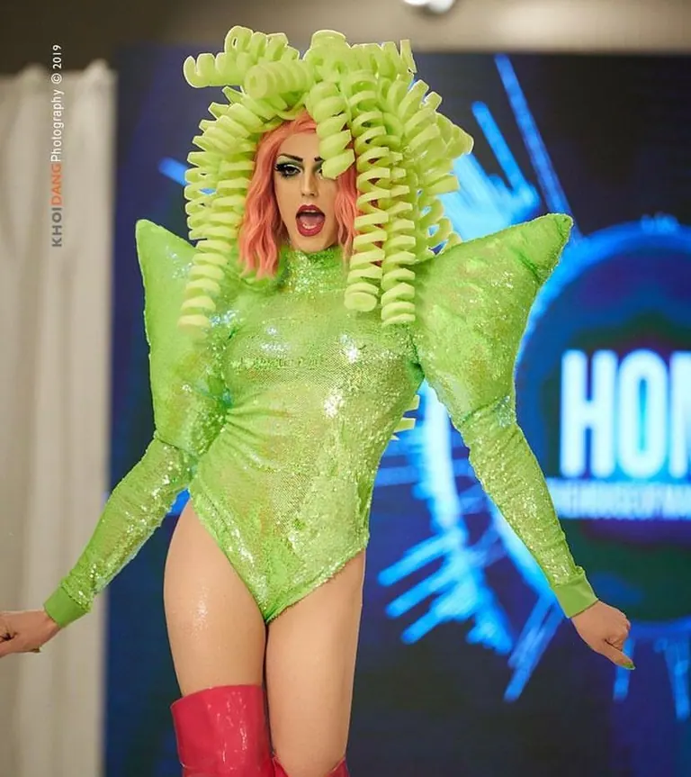 Acid green sequin bodysuit with pointed shoulders and a coiled green wig on a runway