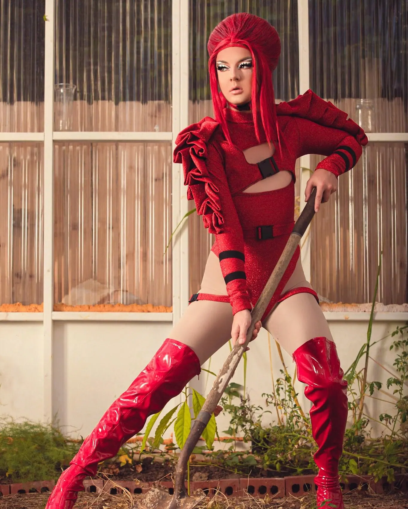 Red ruffled bodysuit and thigh-high boots, posed with a shovel in a garden