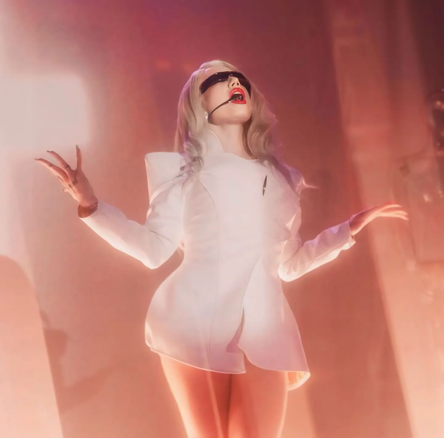 Performer in a white square-shouldered blazer dress on a hazy stage, arms open