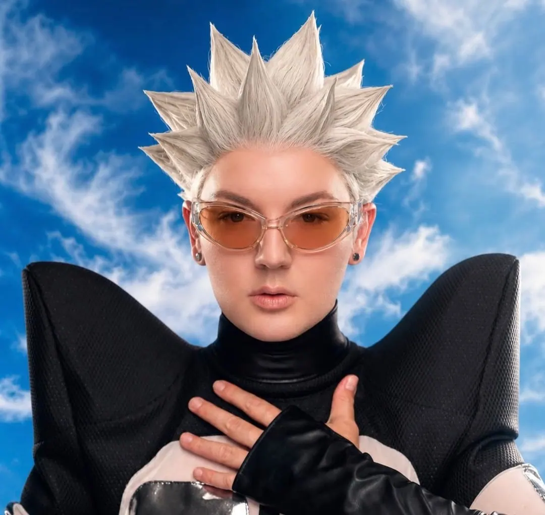 Spiked white wig, amber sunglasses and a black winged-shoulder top against a blue sky